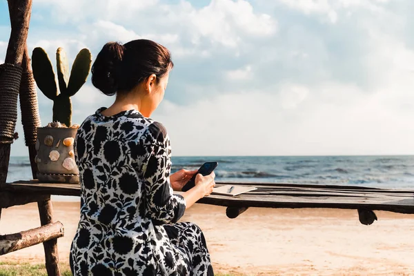Kadın kumsalda akıllı telefon kullanarak masada oturuyor..