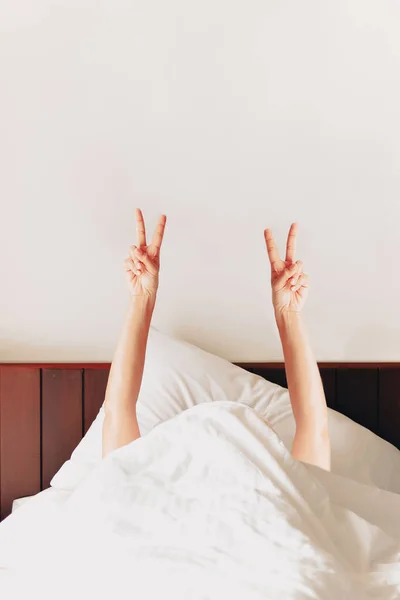 Donna che mostra segno di vittoria con le dita mentre sdraiato sul letto al mattino. — Foto Stock