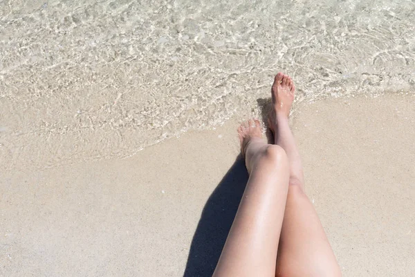 Belle gambe di donna seduta sulla sabbia della spiaggia. — Foto Stock