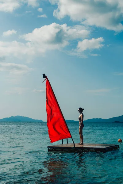 Schöne Frau im Badeanzug mit Sonnenbrille steht auf Holzfloß im Meer. — Stockfoto