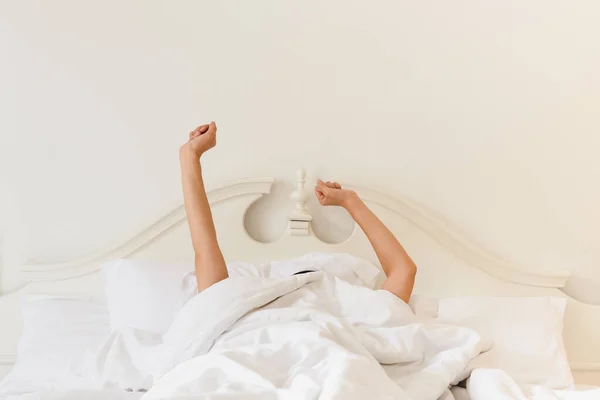 Woman in bed under the blanket stretching hand after waking up. — Foto Stock