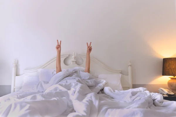 Frau im Bett zeigt ein Siegeszeichen mit zwei erhobenen Händen in der Luft. — Stockfoto