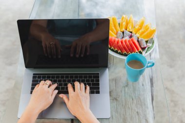 Dizüstü bilgisayarda çalışan bir kadın. Masasında taze meyve ve kahve var..