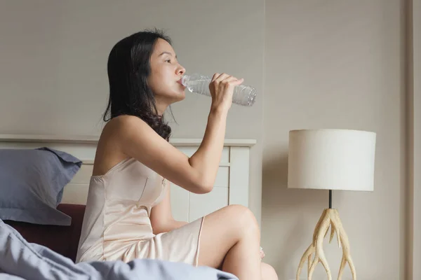 Femme se réveiller le matin assis dans le lit boire de l'eau minérale de la bouteille. — Photo