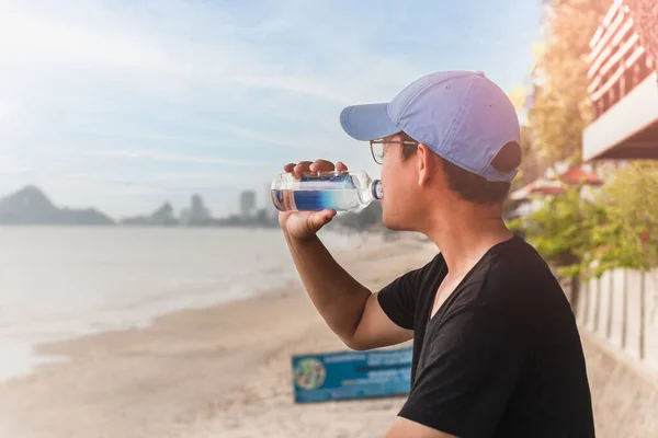 L'homme buvant de l'eau d'une bouteille s'assoit à côté de la plage. — Photo
