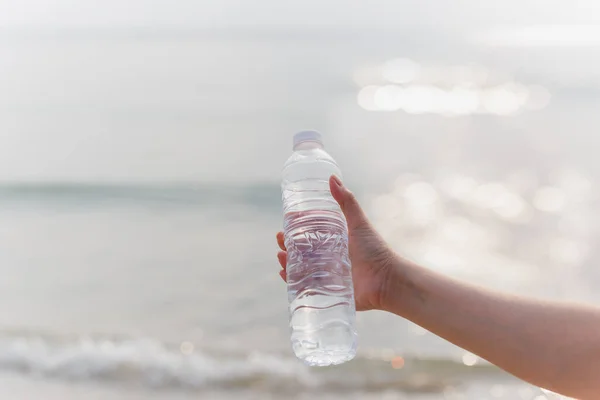 Vrouw met fles mineraalwater in haar hand op het strand. — Stockfoto