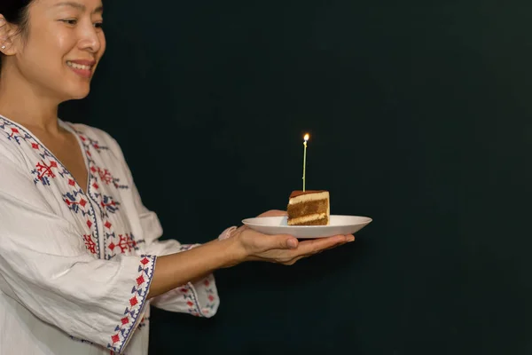 Frau hält ein Stück Geburtstagstorte mit Kerze auf dem Teller. — Stockfoto