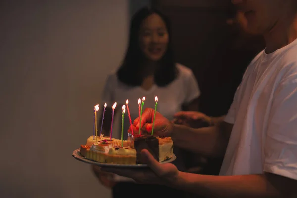 Mann hält Geburtstagstorte mit Kerzen für Geburtstagskind im Haus. — Stockfoto