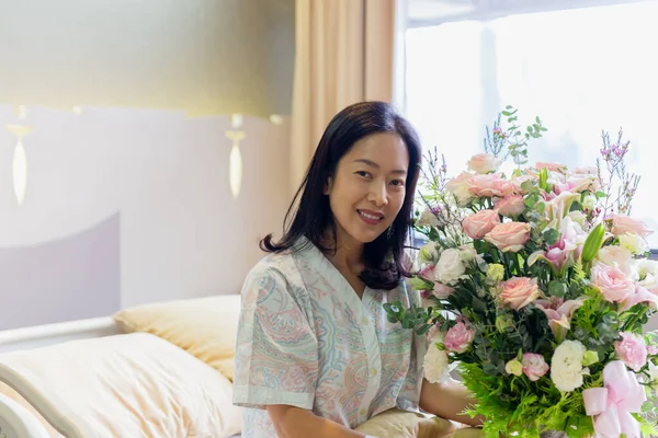 Mujer paciente sonriendo y sosteniendo un ramo de flores sentado en la cama del hospital. — Foto de Stock