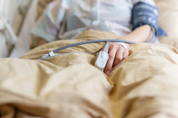 Pacientes asiáticos mano con un oxímetro de pulso conectado en el dedo en la habitación del hospital. — Foto de Stock