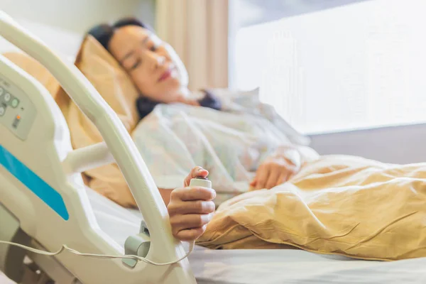 Mujer paciente sosteniendo el botón de llamada de emergencia mientras está acostada en la cama del hospital. — Foto de Stock