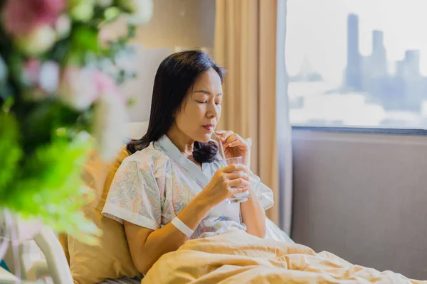 Mujer paciente bebiendo agua mientras está sentada en la cama en el hospital. — Foto de Stock