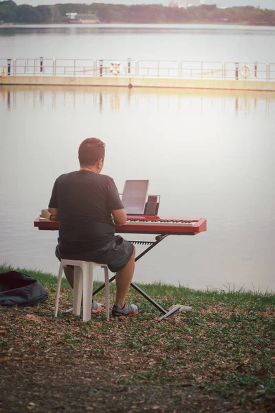 Człowiek grający muzykę fortepianową na syntezatorze nad jeziorem. — Zdjęcie stockowe