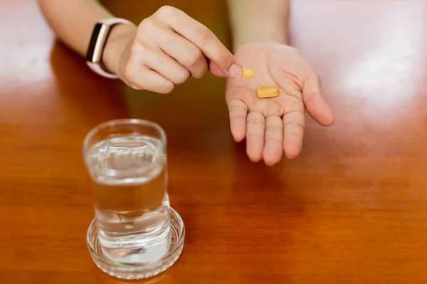 Женские руки с таблетками витамина С и стаканом воды на столе. — стоковое фото