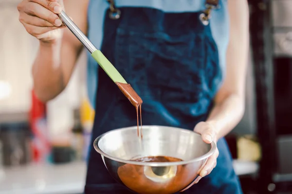 Woman mixing smooth delicious dark chocolate ganache with whisk in silver bowl. — Stock fotografie