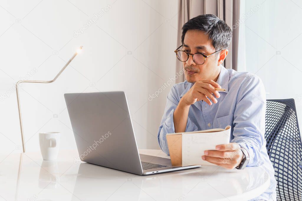 Business man working laptop holding pen and notebook in his hand.