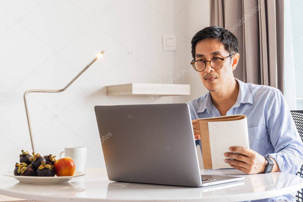 Business man working laptop holding notebook in his hand.