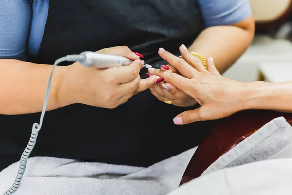 Manicurist is applying electric nail file drill to manicure on female fingers