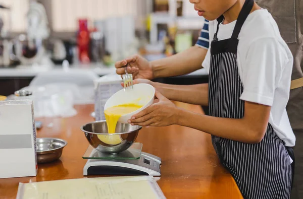 Boy helping mum pouring egg yolks into bowl for baking cake