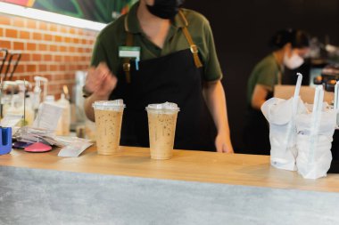 Kafedeki müşteriye buzlu kahve servisi yapan maske takan barista.