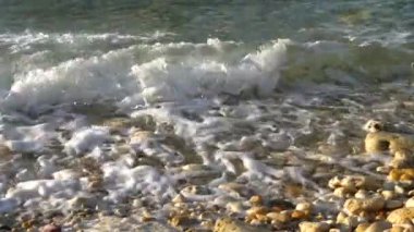 Deniz köpüğü sahili kaplar. Deniz dalgaları çakıl taşlarına çarpıyor.