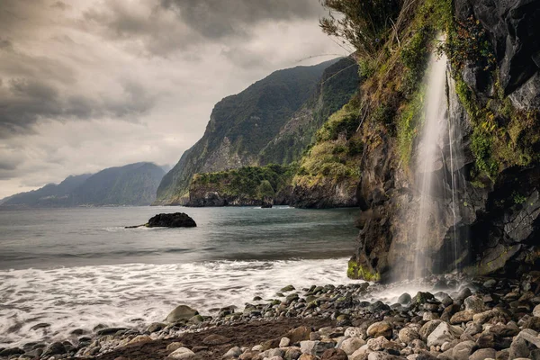 Waterfall in a black sand beach with moody cliffs on the background in Seixal (Madeira, Portugal)