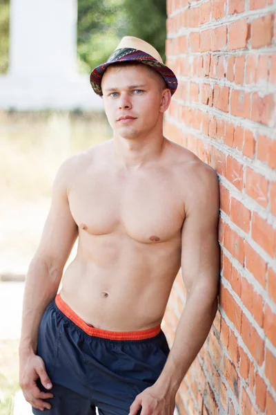 Bodybuilder en un sombrero está parado contra una pared —  Fotos de Stock