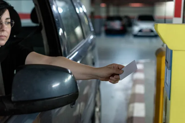 Caucasian woman wearing glasses driving her car approaches the security card to enter the parking lot to the control machine and open the barriers. View from the front. Transport, security.