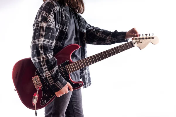 Young man with long hair and dark clothes tunes his red electric guitar. White background.