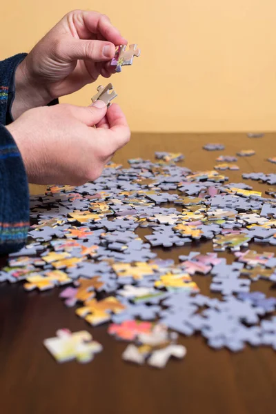 Hands of an adult man in pajamas puts the pieces of a puzzle together. Vertical photo, with selective focus. Hobbies.