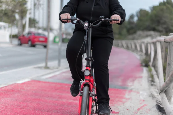 Young teenage girl with real body, climbing a hill with her bicycle. Unrecognizable person.