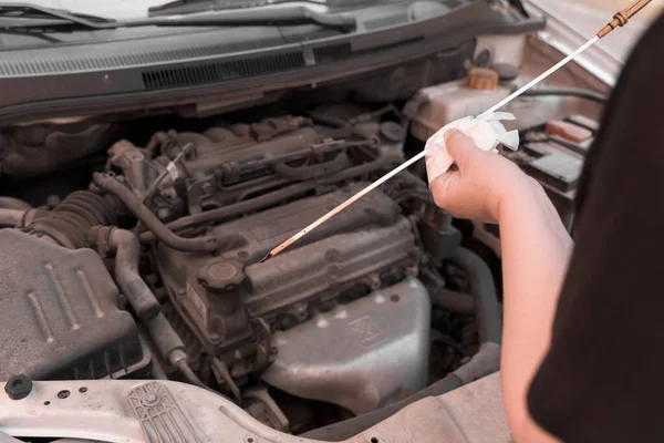 High angle image of a woman\'s hands checking the oil level of a car with an oil dipstick. The car engine is out of focus in the background.