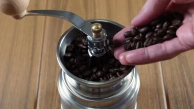 Carefully pouring coffee beans into a manual hand coffee grinder
