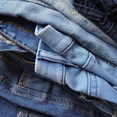 Stack of pairs of denim jeans of various blue shades and sizes