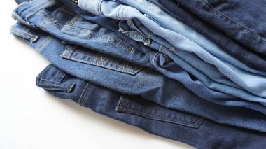 Stack of pairs of denim jeans of various blue shades and sizes