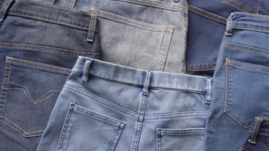 Close up pan shot of pairs of denim jeans back side of various blue shades and sizes