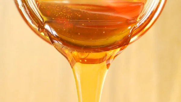 Close up shot of honey pouring out of glass jar. Health and beauty product sustainable lifestyle concept.