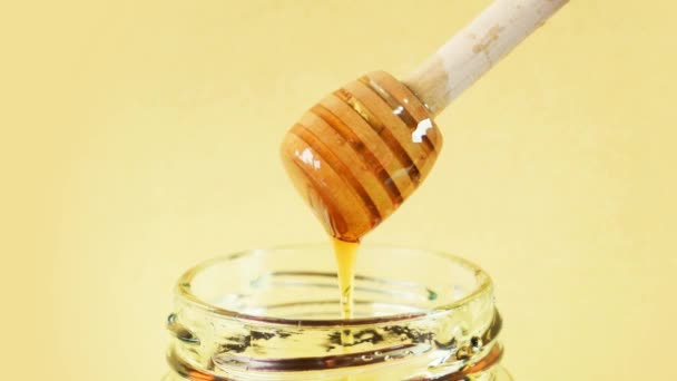 蜂蜜从蜂蜜搅拌器中滴落在有普通背景的玻璃瓶中 — 图库视频影像