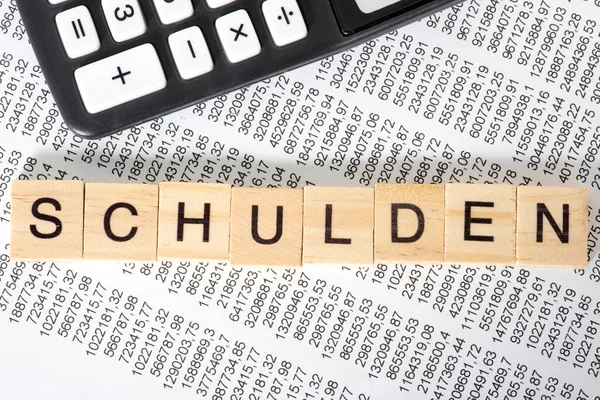 在木制立方体 财务文件和背景计算器上写的Schulden字 — 图库照片