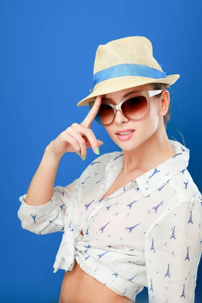 Giovane donna in cappello e occhiali da sole, isolata su sfondo blu — Foto Stock