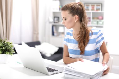 Elinde evrakları olan kadın masanın üstünde oturuyor.