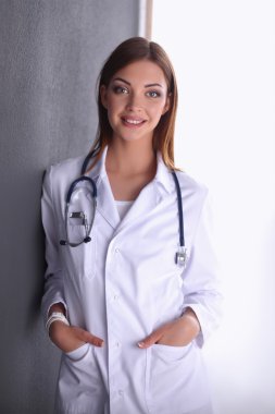Steteskoplu doktor kadın gri duvarın yanında duruyor.
