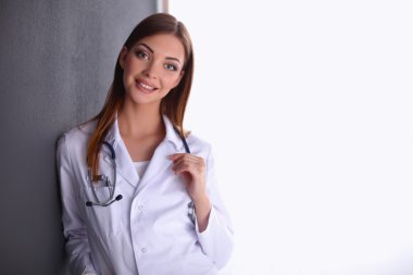 Steteskoplu doktor kadın gri duvarın yanında duruyor.