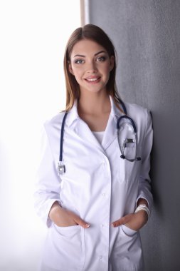 Steteskoplu doktor kadın gri duvarın yanında duruyor.