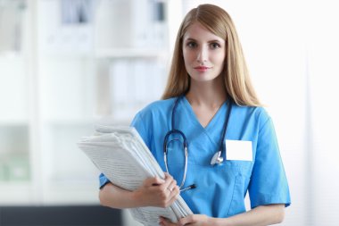 Hastane koridorunda klasörlü kadın doktor portresi.