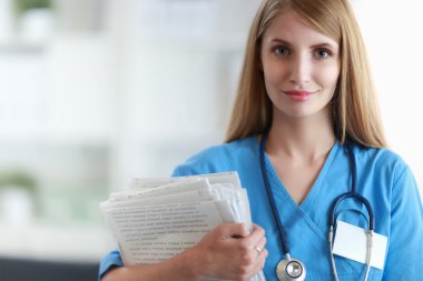 Hastane koridorunda klasörlü kadın doktor portresi.