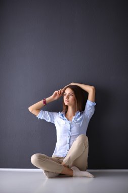 Genç bir kadın yerde, kara duvarın yanında oturuyor.