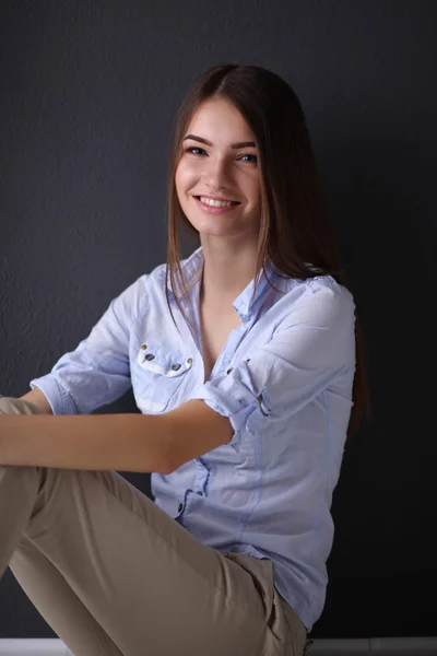 Mujer joven sentada en el suelo cerca de la pared oscura, fondo gris aislado —  Fotos de Stock