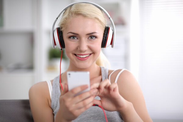 Young beautiful woman at home sitting on sofa and listening music