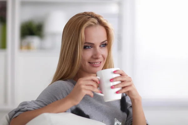 Giovane bella donna con una tazza sul divano a casa — Foto Stock